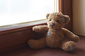 Cute little teddy bear toy sitting on brown wooden window sill with copy space for text on window glass.