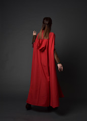 Naklejka na ściany i meble full length portrait of brunette girl wearing red medieval costume and cloak. standing pose with back to the camera on grey studio background.