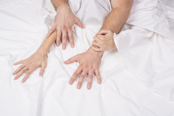 Fototapeta na wymiar Close up of passionate couple hold hands during making intense love in bedroom, lovers enjoy hot sex on white sheet, boyfriend and girlfriend relax having intimacy at home, reaching orgasm or ecstasy.