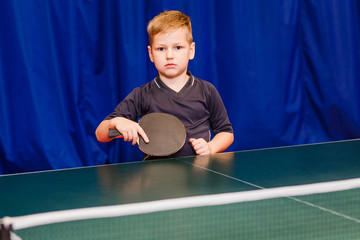 seven years boy holding a black racket for table tennis indoors