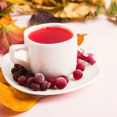 Autumn composition with red healthy cranberry hot drink and dry decoration leaves over pink background