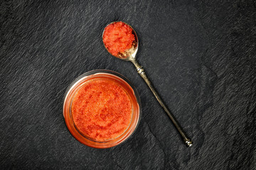An overhead photo of red caviar in a jar and in a spoon, shot from above on a black background with a place for text