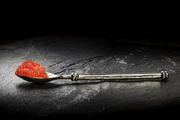 A photo of red caviar in a spoon, side view on a black background with a place for text