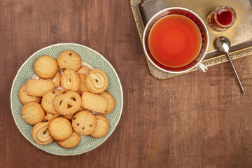 An overhead photo of Danish butter cookies on a plate, on a dark rustic background with a cup of tea on a vintage tray, with jam, and copy space