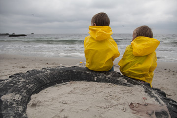 Two children in yellow clothes sit on the beach and look to one side.