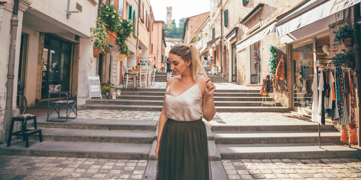 Europe fun, summer happy romantic woman in vacation in Italy, Santarcangelo Di Romagna - portrait of curvy blonde hair woman walking in typical italian old city center - travel and relaxing concept