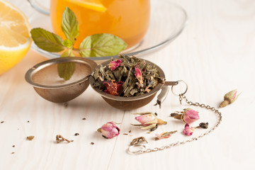 Closeup of cup of tea with tea leaves, mint on vintage wooden background. Black herbal tea with lemon, ginger and honey. hot winter drink