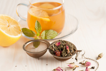 Closeup of cup of tea with tea leaves, mint on vintage wooden background. Black herbal tea with lemon, ginger and honey. hot winter drink