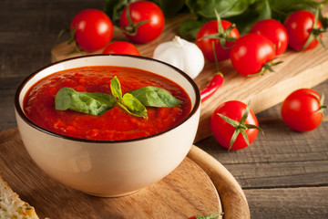 Fresh, healthy tomato soup with basil, pepper, garlic, tomatoes and bread on wooden background. Spanish gazpacho soup.