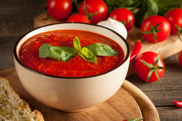 Fresh, healthy tomato soup with basil, pepper, garlic, tomatoes and bread on wooden background. Spanish gazpacho soup.