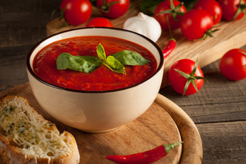 Fresh, healthy tomato soup with basil, pepper, garlic, tomatoes and bread on wooden background. Spanish gazpacho soup.
