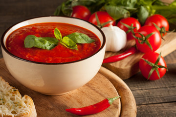 Fresh, healthy tomato soup with basil, pepper, garlic, tomatoes and bread on wooden background. Spanish gazpacho soup.