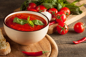 Fresh, healthy tomato soup with basil, pepper, garlic, tomatoes and bread on wooden background. Spanish gazpacho soup.