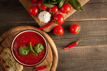 Fresh, healthy tomato soup with basil, pepper, garlic, tomatoes and bread on wooden background. Spanish gazpacho soup.