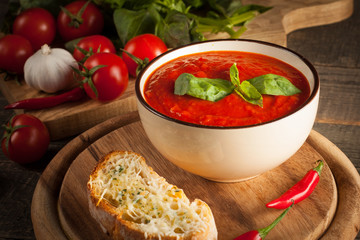 Fresh, healthy tomato soup with basil, pepper, garlic, tomatoes and bread on wooden background. Spanish gazpacho soup.