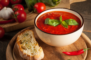 Fresh, healthy tomato soup with basil, pepper, garlic, tomatoes and bread on wooden background. Spanish gazpacho soup.