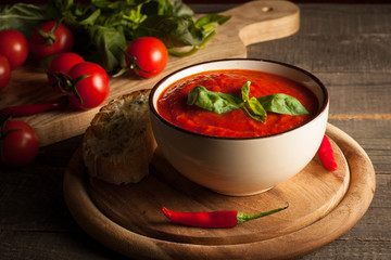 Fresh, healthy tomato soup with basil, pepper, garlic, tomatoes and bread on wooden background. Spanish gazpacho soup.