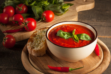 Fresh, healthy tomato soup with basil, pepper, garlic, tomatoes and bread on wooden background. Spanish gazpacho soup.