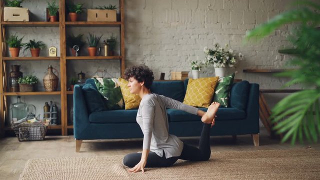 Attractive young woman is stretching legs and arms sitting on floor during individual practice at home. Healthy lifestyle, interior and people concept.