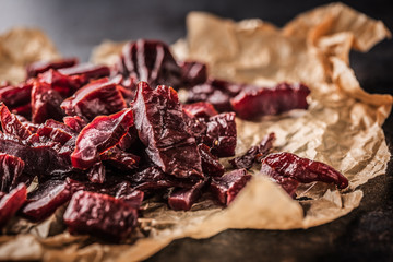 A pile of dried beef jerky pieces on paper and cutting board - obrazy, fototapety, plakaty
