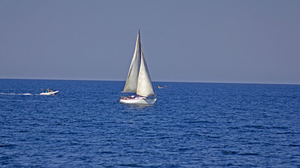 Fototapeta premium White sailboat on a background of blue sea. Sailing boat with a white sail in the blue sea in summer. 