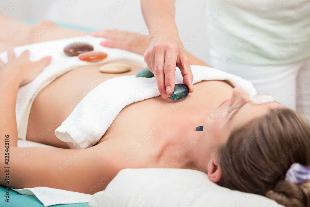 Wall mural Therapist placing stones on woman's body in spa