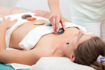 Fototapeta na wymiar Therapist placing stones on woman's body in spa