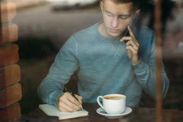A young business man working and drinking coffee in a cafe and write down something in the notebook