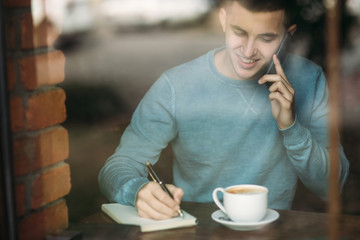 Man with phone in a cafe sits opposite the window. Talking on the phone. View from the window