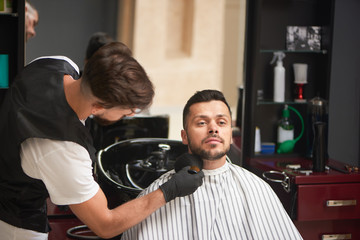 Male hairdresser grooming client's beard with brush.