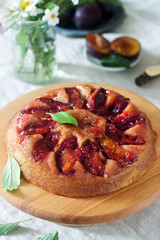 Sweet cake with caramelized plums, plums and a bouquet of flowers on the table. Rustic style.
