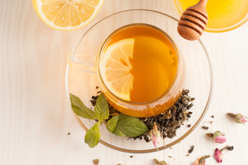 Closeup of cup of tea with tea leaves, mint on vintage wooden background. Black herbal tea with lemon, ginger and honey. hot winter drink