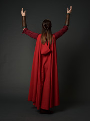 Fototapeta premium full length portrait of brunette girl wearing red medieval costume and cloak. standing pose with back to the camera on grey studio background.