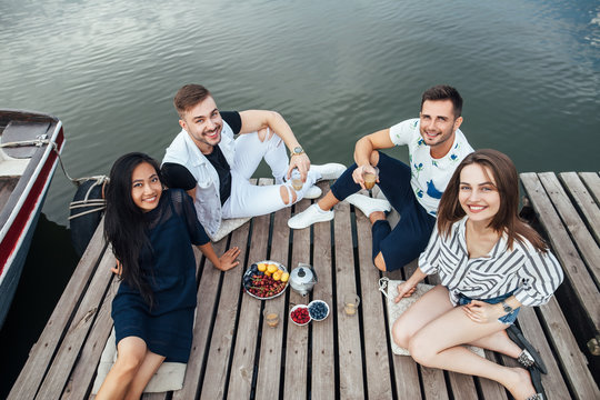 Group of happy young friends relaxing on river wooden pier