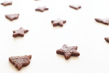 Gingerbread cookie in the shape of stars and fir trees with icing sugar on a white background. Christmas pattern in the style of minimalism