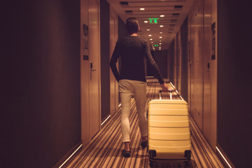 Rear view of man with suitcase walking in hotel lobby.