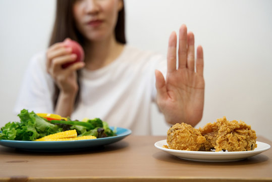 Young Girl On Dieting For Good Health Concept. Close Up Female Using Hand Reject Junk Food By Pushing Out Her Favorite Fried Chicken And Choose Red Apple And Salad For Good Health.