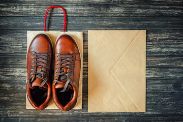 brown leather men's boots and kraft envelope on a wooden background, top view
