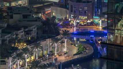 Fototapeta premium Promenade and canal in Dubai Marina with luxury skyscrapers and yachts around night timelapse, United Arab Emirates