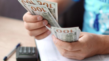 Male hands counting dollars banknotes above tax form.