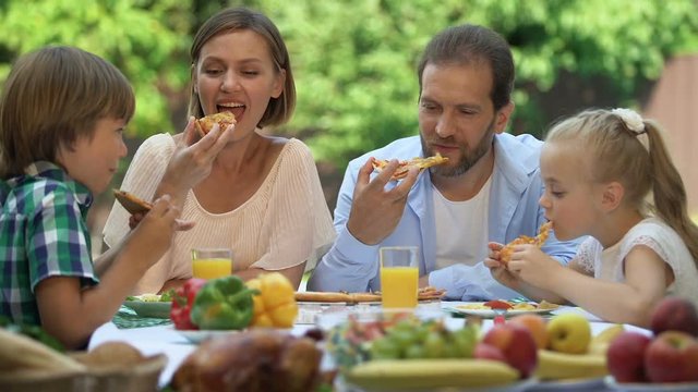 Happy family having lunch together, children eating pizza, parents smiling