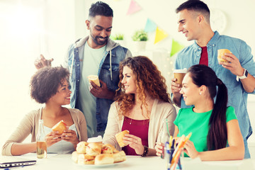 corporate, celebration and people concept - happy friends or team eating sandwiches with coffee and non-alcoholic drinks at office party