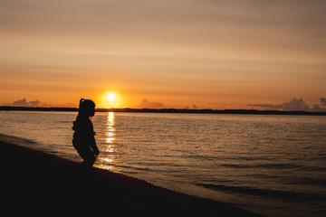 Fototapeta premium silhouette of a child on the background of the setting sun on the beach