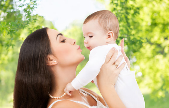 family and motherhood concept - happy smiling young mother kissing little baby over green natural background