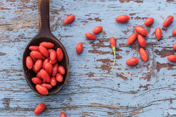Goji raw berries in the wooden spoon and on the blue wooden background, healthy eating and health concept