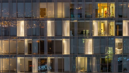Windows of the multi-storey building of glass and steel lighting inside and moving people within timelapse