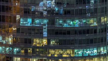 Windows of the multi-storey building of glass and steel lighting inside and moving people within timelapse