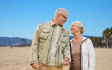 old age, travel and tourism and people concept - happy senior couple holding hands over venice beach background in california