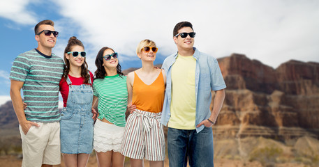 travel, tourism and summer holidays concept - group of happy smiling friends in sunglasses hugging over grand canyon national park background