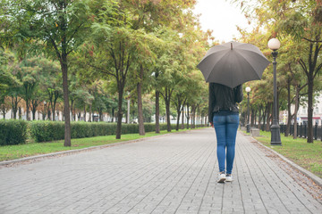 girl in a black leather jacket and blue jeans with a black umbrella in her hands on the mall